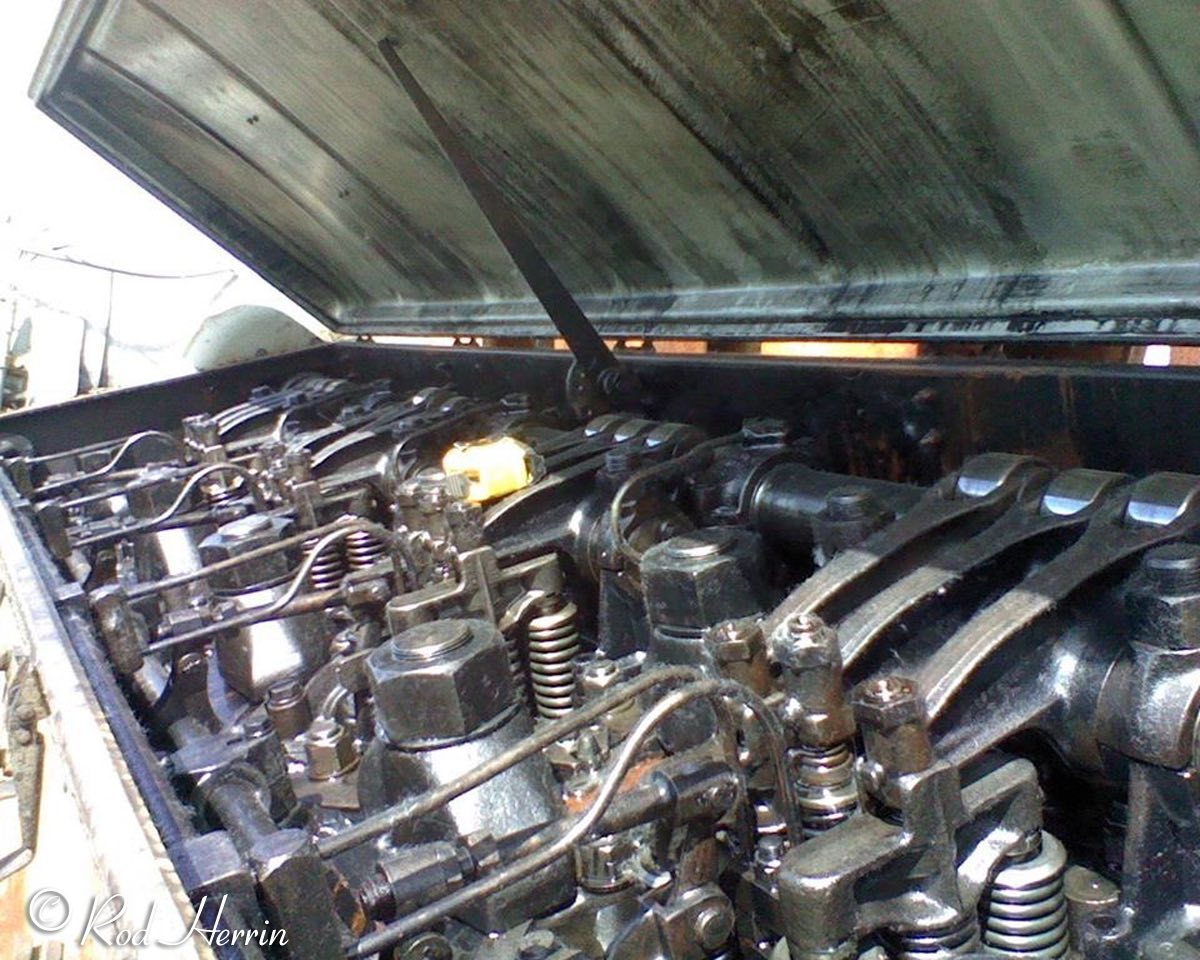 Note the size of the yellow tape measure. You can see the valve springs and fuel supply / return tubes. Camshaft at the right with 3 roller rocker arms per cylinder riding on the lobes.